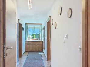A hallway with a wooden door on the left, a window with curtains, and a sink area with cabinets. - Tobias 3 by Interhome (Radstadt)