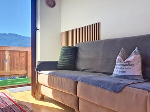 Un canapé avec un coussin et un oreiller, un mur fait de lattes de bois, et une vue sur une clôture en bois et des montagnes.