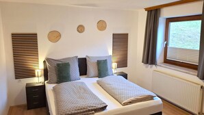 A bedroom with a large bed, two bedside tables, a window with curtains, and wall-mounted decorative items.