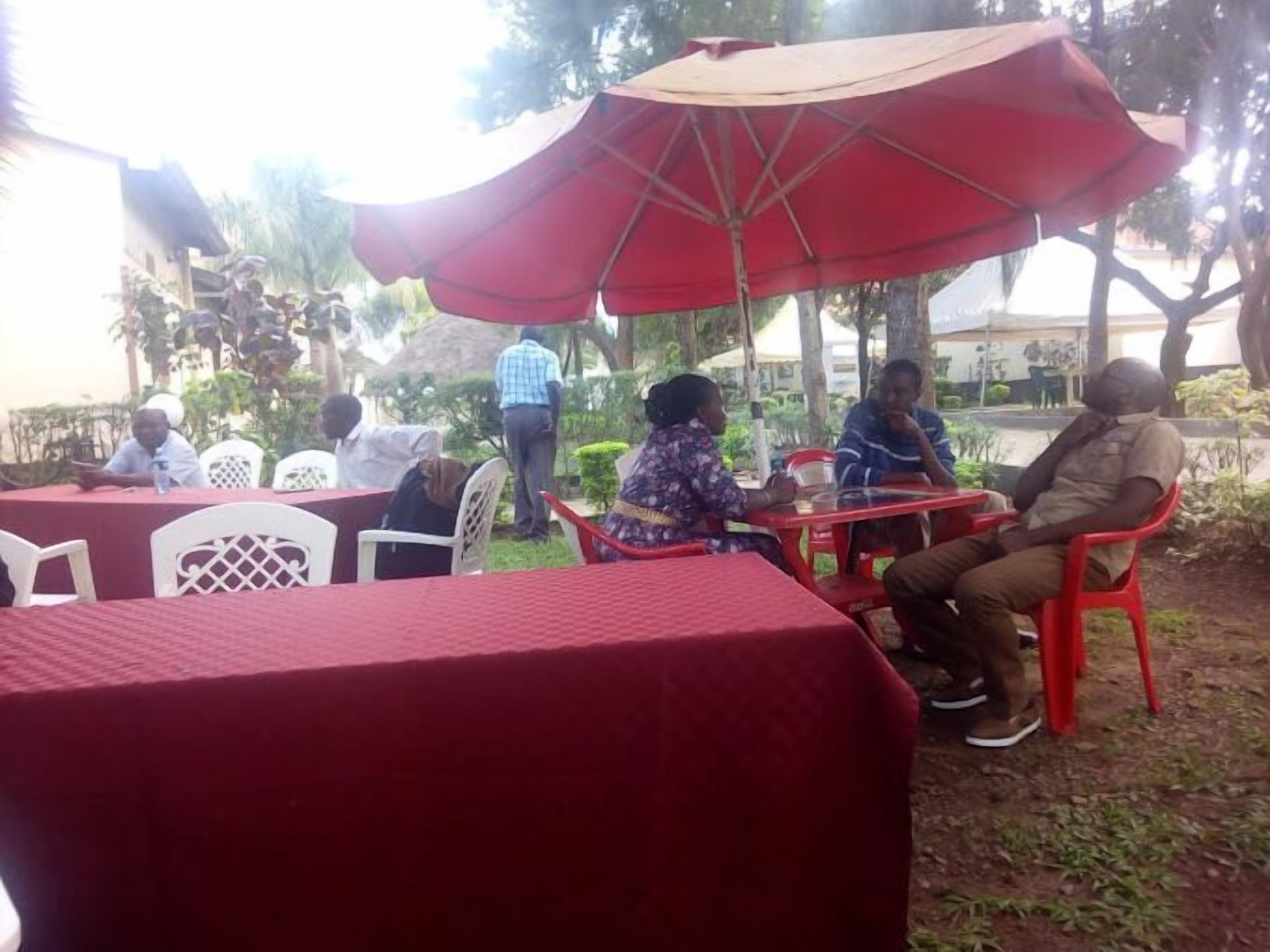 An outdoor seating area with red tables and chairs, covered by a large red umbrella.