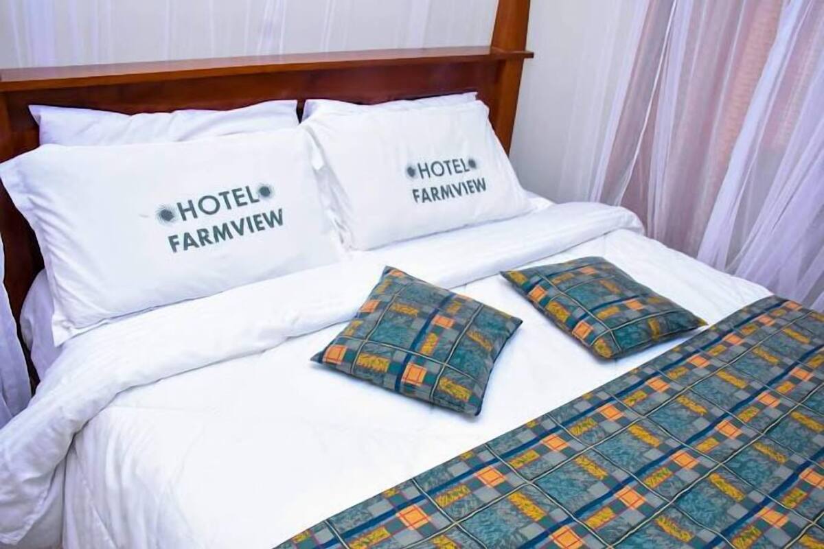 Uma cama bem arrumada com roupa de cama e almofadas brancas com a inscrição "HOTEL FARMVIEW".
