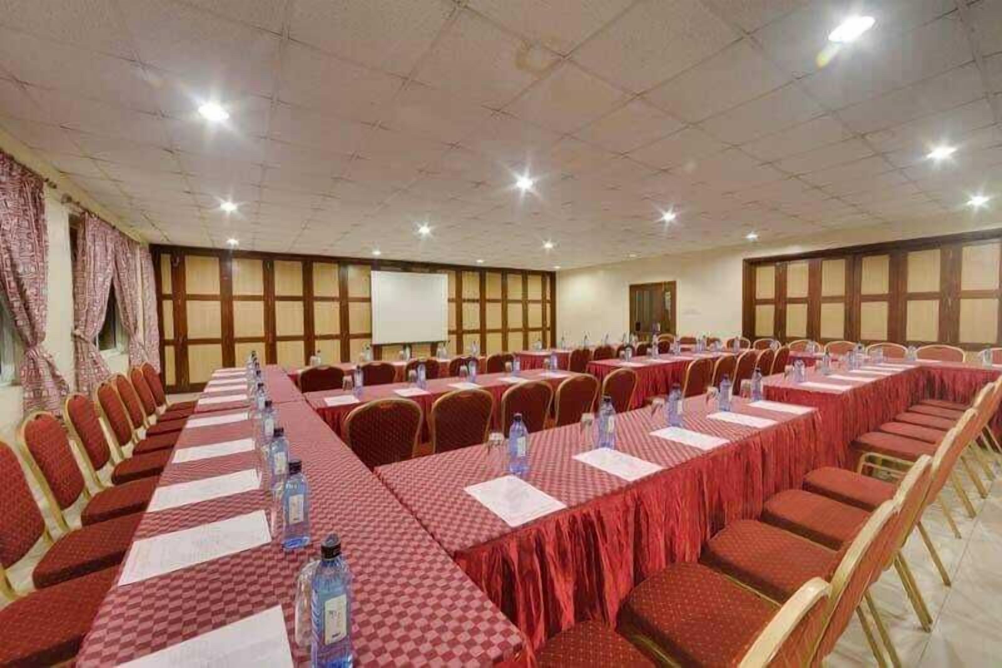 A conference room with long tables, chairs, and a projector screen.
