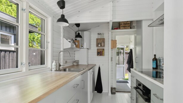 A modern kitchen with white cabinetry, a wooden countertop, and a black hanging light fixture.