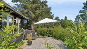 A wooden deck with a white umbrella, potted plants, and a grill area.
