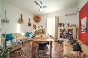 Un soggiorno con zona pranzo, una ventola a soffitto, chitarre e una libreria.