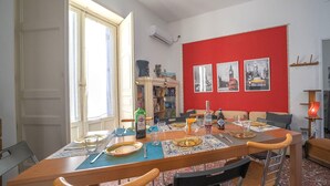 A dining area with a table set for four, a bookshelf, and a red accent wall with framed pictures.
