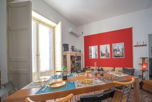 A dining area with a table set for four, a bookshelf, and a red accent wall with framed pictures. - Historic Sicilian Home for 10 Guests with Balconies in Old Town Catania (Catania)