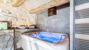 Un espace spa doté d’un jacuzzi, de murs en pierre et d’un plafond en bois.