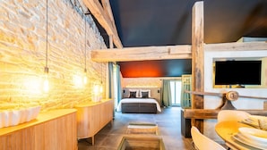 Un intérieur moderne avec des murs en briques apparentes, un banc en bois, un lit et un coin repas équipé d’un téléviseur.