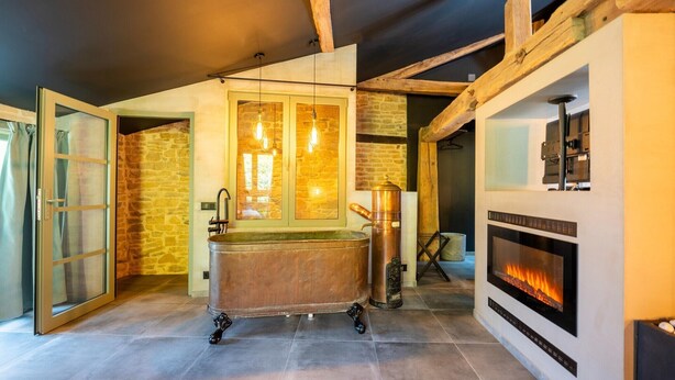 A modern interior with a stone wall, a bathtub on wheels, a fireplace, and hanging light fixtures. - Holiday Home in Sainte-Cécile with Sauna (Saint-Cecile)