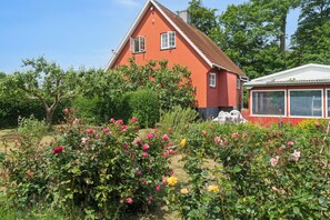 Une maison rouge avec une fenêtre blanche, entourée d’une végétation luxuriante et de fleurs en pleine floraison.