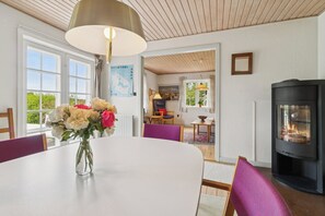 Un coin repas comprenant une table, des chaises, un vase de fleurs, une cheminée et une vue sur la verdure à l’extérieur.
