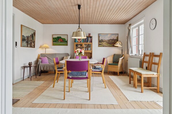 Un salon chaleureux avec un plafond en bois, une table à manger avec des chaises, un canapé, une bibliothèque et une fenêtre avec une horloge.