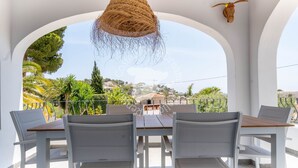 Una terraza con muebles blancos, un colgante de luz tejido y una decoración con cabeza de toro.