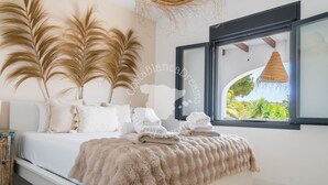 Un dormitorio con cama, almohadas, una ventana y vistas al verde exterior.