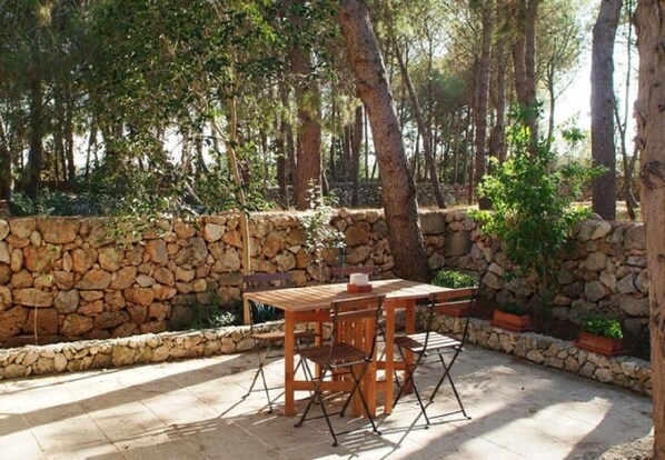 An outdoor patio with a stone wall, a wooden table, and chairs. - Masseria Frassaniti (Veglie)
