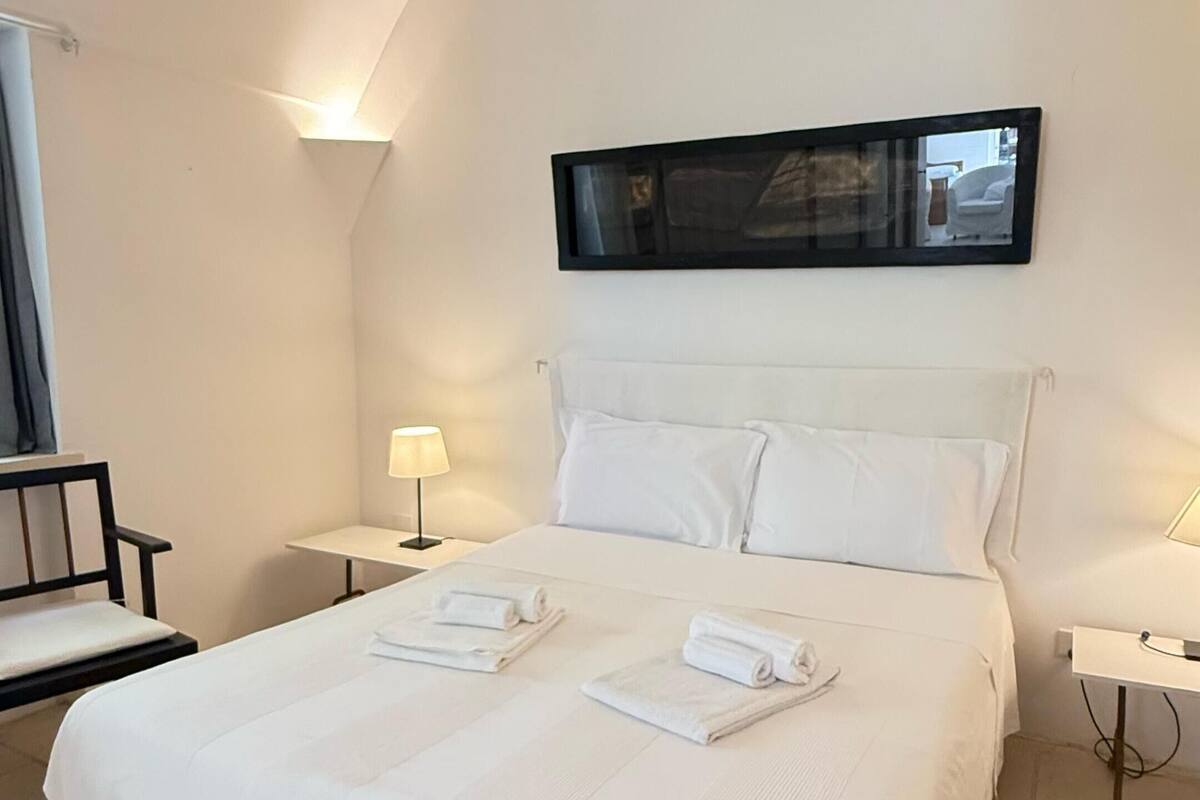Ein Hotelzimmer mit einem großen Bett, zwei Nachttischen mit Lampen, einem Sessel und einem an der Wand montierten Fernseher.