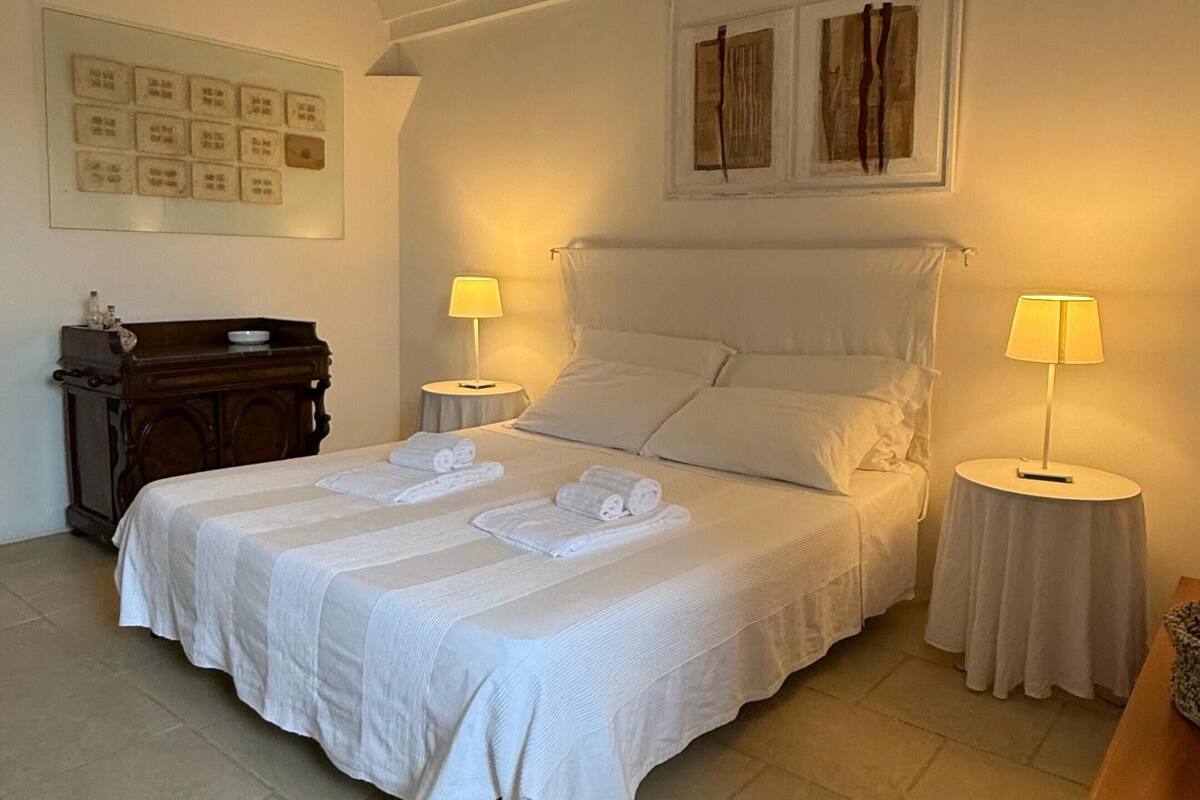 Ein ordentlich eingerichtetes Schlafzimmer mit einem Bett, zwei Nachttischen, einem Beistelltisch und einer Holzkommode.