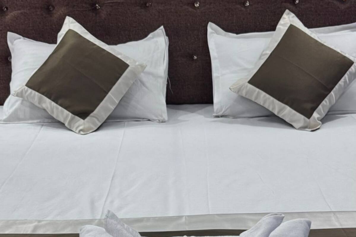 A neatly made bed with white linens and a folded towel, a tufted headboard, and two pillows with a dark accent.