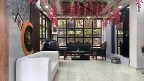 A room with a sofa, a white chair, and a green sofa set. There are large windows with a view of greenery outside. - Hotel Bless Inn (Patna)