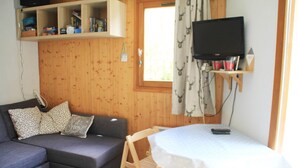A cozy room with a grey sofa, a small table with a white tablecloth, a television mounted on the wall, and wooden paneling. - Holiday home in Chatel near ski area (Châtel)