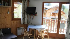 A cozy room with a wooden interior, a TV mounted on the wall, a small table with a tablecloth, and a balcony with a railing. - Holiday home in Chatel near ski area (Châtel)