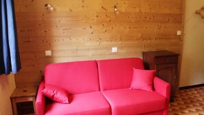 A room with a wooden wall, a red sofa, a small wooden cabinet, and a patterned floor. - Apartment for 2 with mountain views (Châtel)