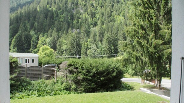A view from a window of a building with a grassy yard, a wooden fence, and a forested hillside in the background. - Apartment for 2 with mountain views (Châtel)