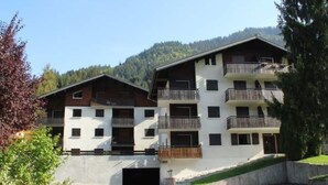 A multi-story building with balconies, a garage, and a mountainous backdrop. - Apartment for 2 with mountain views (Châtel)