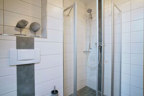 A modern bathroom with a glass-enclosed shower, a marble sink, and a small shelf with decorative shells.
