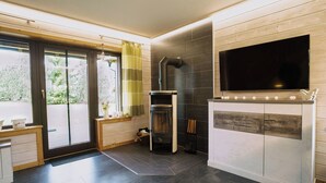 A modern kitchen with a built-in fireplace, a large flat-screen TV, and a sliding glass door leading to a balcony. - Your Holiday Home With Fireplace in the Harz (Oberharz am Brocken)