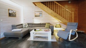 A modern living room with a wooden staircase, a grey sofa, a white coffee table, and a rocking chair. - Your Holiday Home With Fireplace in the Harz (Oberharz am Brocken)