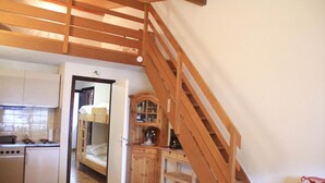 A compact kitchen with a stove, sink, and a small refrigerator. There is a wooden staircase leading to an upper level.