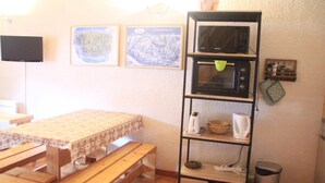 A kitchen with a wooden table and benches, a microwave shelf, and two framed pictures on the wall.