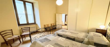 A bedroom with two beds, a window, a chair, and a bedside table with a lamp.