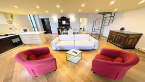 Ein modernes Wohnzimmer mit einem weißen Sofa, zwei roten Sesseln, einem Couchtisch und einer Treppe, die zu einer oberen Ebene führt.