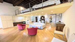 Un'ampia zona giorno con soffitto alto, una cucina, un'area pranzo e una scala che conduce a un livello superiore.