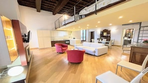 A spacious living area with a high ceiling, wooden flooring, a white sofa, a red armchair, and a dining area with a table and chairs. - 6 Guests apt With Terrace in Pedestrian Historic Centre of Spoleto (Spoleto)