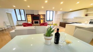 A modern living room with a white sofa, red chairs, and a dining table with a wine bottle and glasses. - 6 Guests apt With Terrace in Pedestrian Historic Centre of Spoleto (Spoleto)