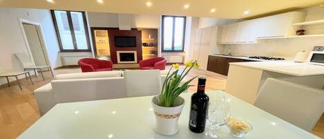A modern living room with a white sofa, red chairs, and a dining table with a wine bottle and glasses.