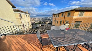 Une terrasse avec une table et des chaises, offrant une vue sur un paysage urbain avec des bâtiments et des montagnes.