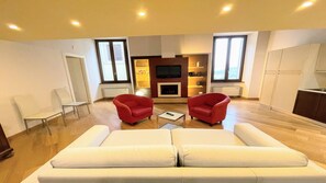 Ein modernes Wohnzimmer mit einer Couch, zwei roten Sesseln, einem Couchtisch, einem Fernseher und einem Kamin.