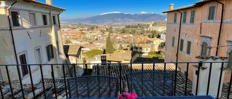 A balcony with a table and chairs, overlooking a town with buildings and a mountain in the distance.