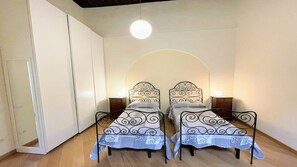 A room with two metal beds with ornate headboards, a white wardrobe, and a round ceiling light.