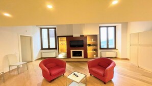 A living room with two red armchairs, a coffee table, a TV, and a fireplace. - 6 Guests apt With Terrace in Pedestrian Historic Centre of Spoleto (Spoleto)