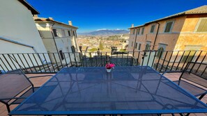 Una terrazza con un tavolo e sedie in metallo, una pianta in vaso e vista su una città con montagne sullo sfondo.