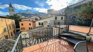 A rooftop terrace with a metal railing, a view of historic buildings, and a stone wall. - 6 Guests apt With Terrace in Pedestrian Historic Centre of Spoleto (Spoleto)
