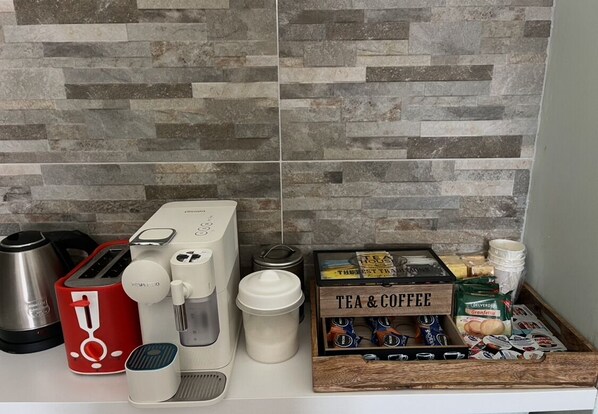 A kitchen counter with a coffee maker, toaster, kettle, and a box of tea and coffee. - VillaRealeFlats (Lecce)