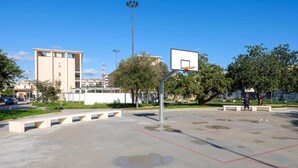 An outdoor basketball court with a basketball hoop, benches, and trees. - VillaRealeFlats (Lecce)