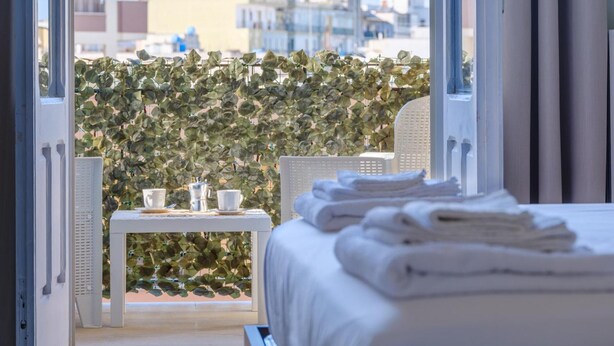 A hotel room with a bed, a small table with cups and a coffee pot, and a view of buildings through a window. - VillaRealeFlats (Lecce)
